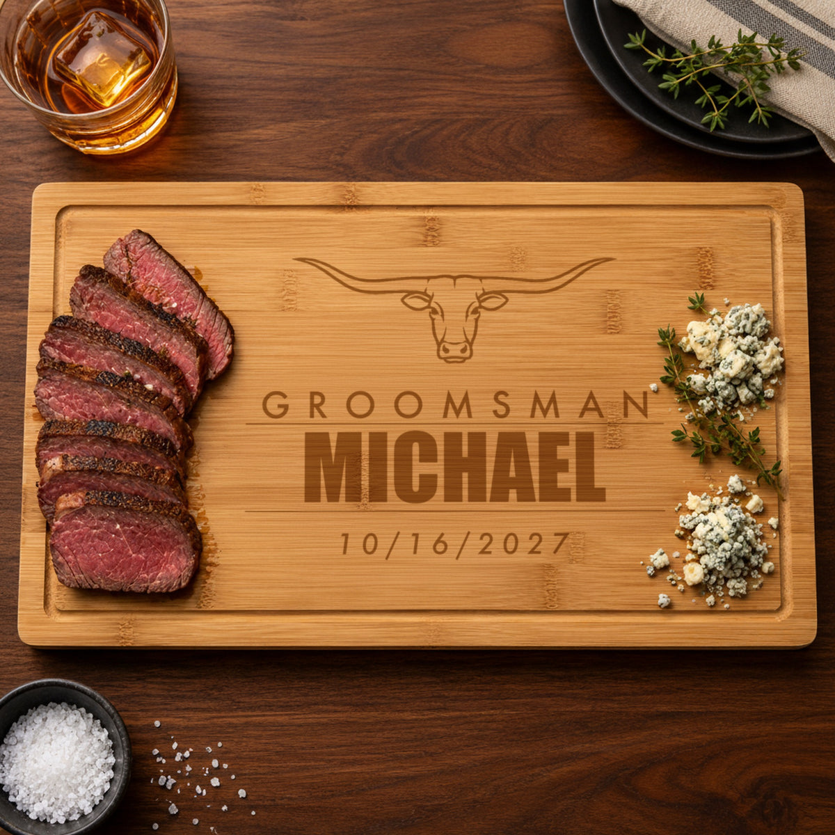 Personalized steakhouse cutting board engraved as a groomsman gift with Groomsman, the name Michael and the wedding date 10/16/2027 under a longhorn steer