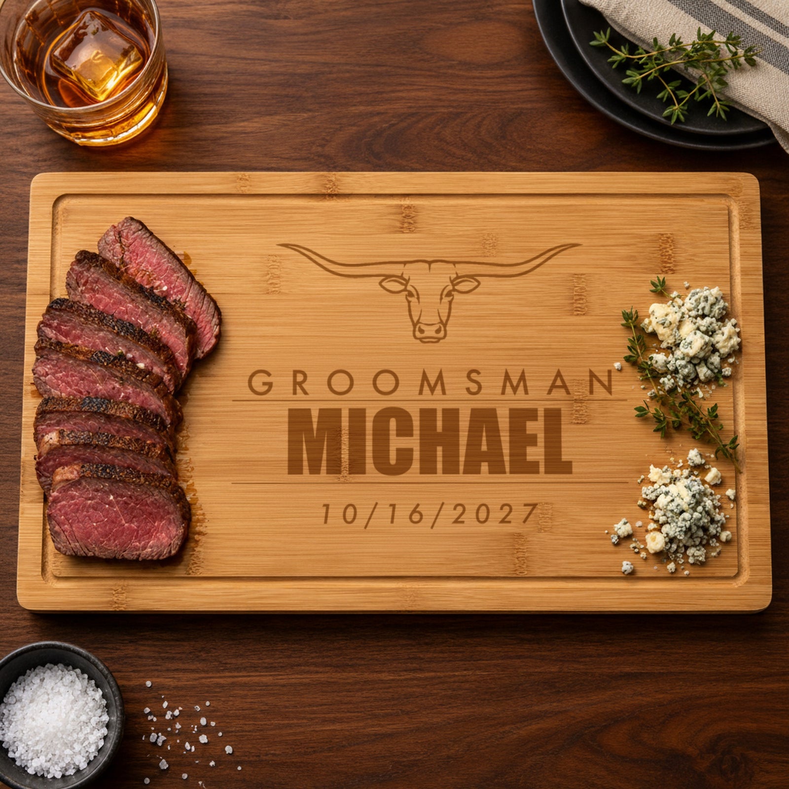 Personalized steakhouse cutting board engraved as a groomsman gift with Groomsman, the name Michael and the wedding date 10/16/2027 under a longhorn steer