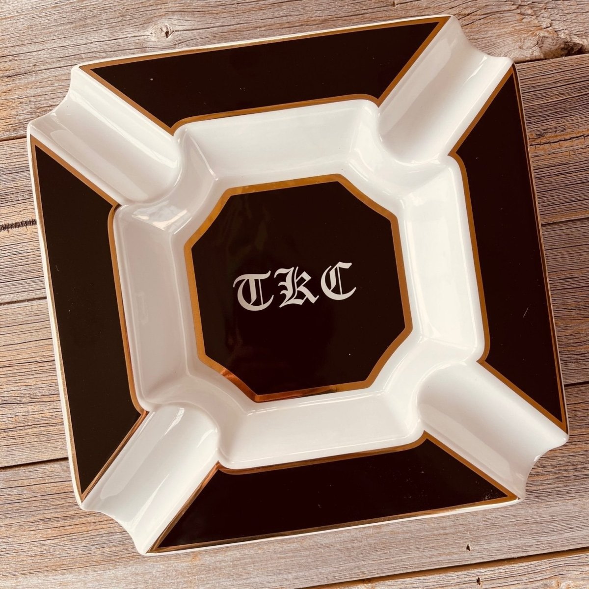 Top-down look at a large personalized cigar ashtray with four cigar rests, a deep white basin and the initials TKC on the black octagon in the middle