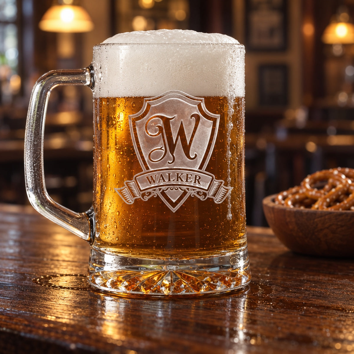 Personalized beer mug sand-carved with a shield crest, a large W initial and WALKER on a ribbon banner, full of lager on a dark wood pub bar beside pretzels.