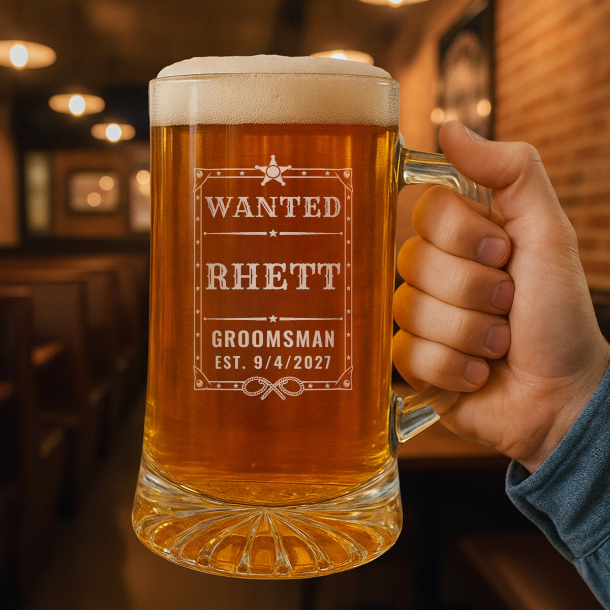 Hand holding the 25 oz personalized wanted poster beer stein in a pub, engraved with an Old West wanted poster with a sheriff star and lassos: Wanted, Rhett, Groomsman